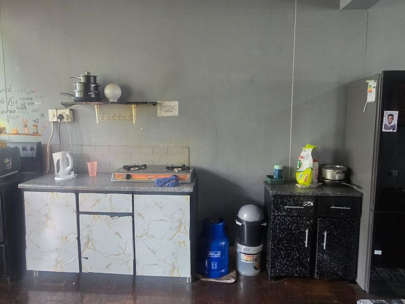 A functional kitchen area featuring basic cabinetry, a gas hob, and tiled splashback, currently showing signs of wear and dated finishes.