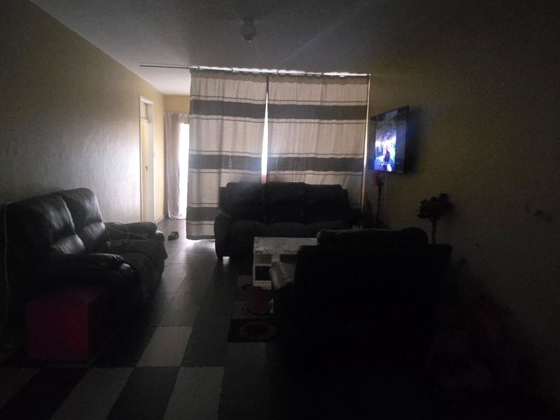 A dimly lit living room featuring tiled flooring and a curtained window area, requiring improved lighting and cosmetic updates to enhance the space.