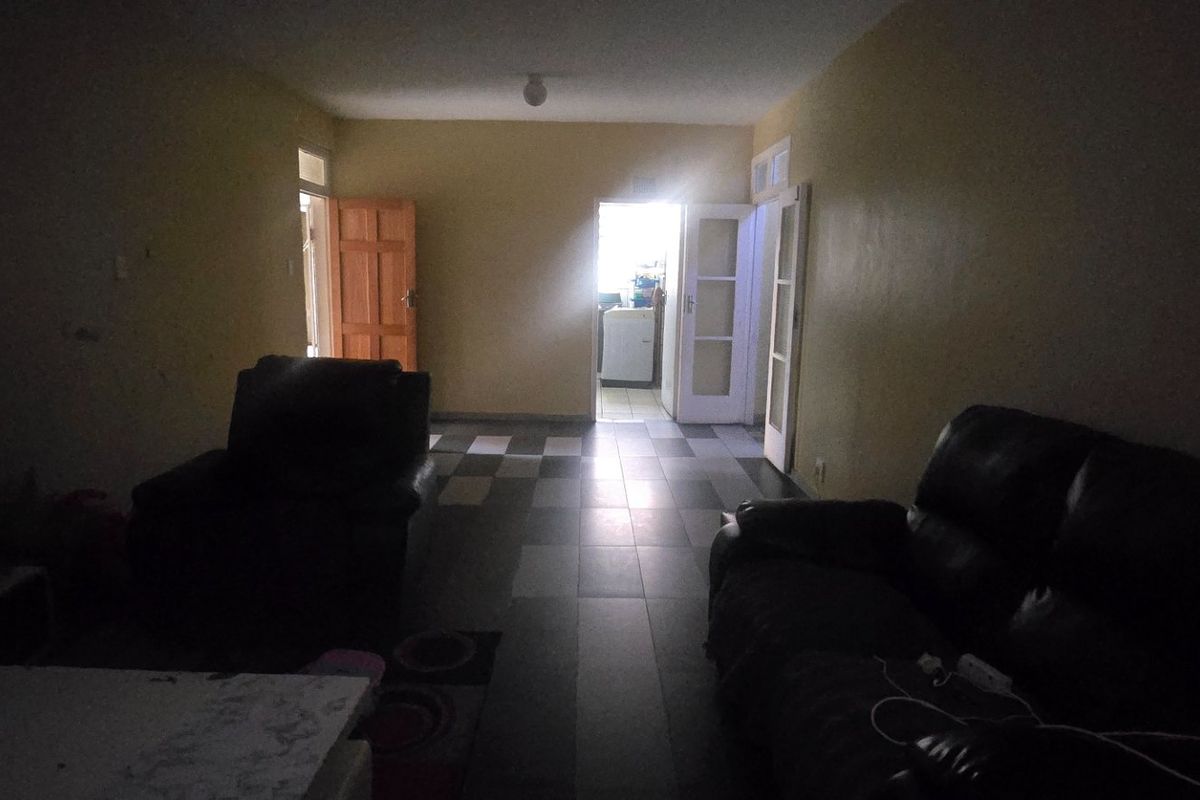 A dimly lit living room featuring tiled flooring and access to adjacent rooms, requiring improved lighting and cosmetic updates to enhance the space.