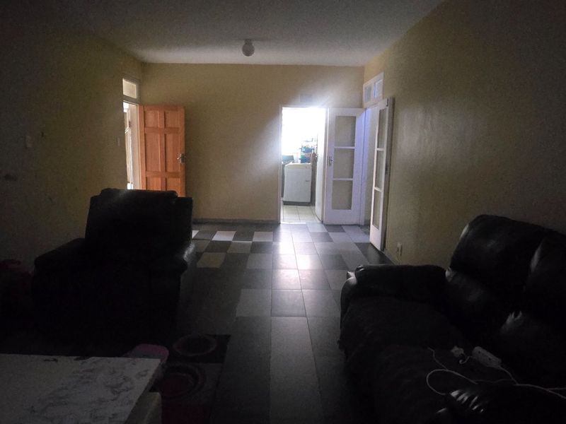 A dimly lit living room featuring tiled flooring and access to adjacent rooms, requiring improved lighting and cosmetic updates to enhance the space.