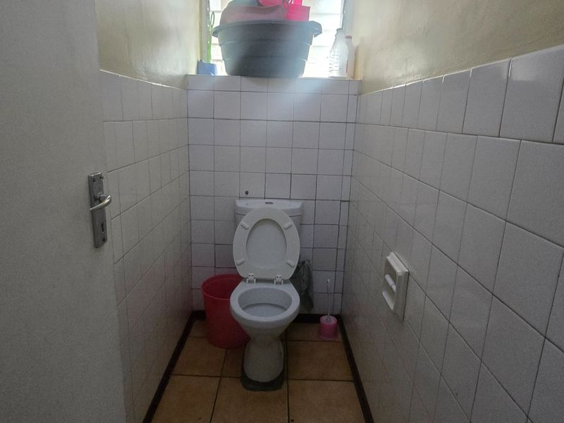 A compact bathroom featuring white wall tiles, tiled flooring, and a standard toilet, requiring cosmetic updates to improve its overall condition.