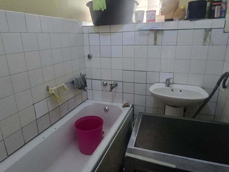 A compact bathroom featuring a bathtub and pedestal basin with tiled walls. The space requires maintenance and cosmetic updates to improve its condition.