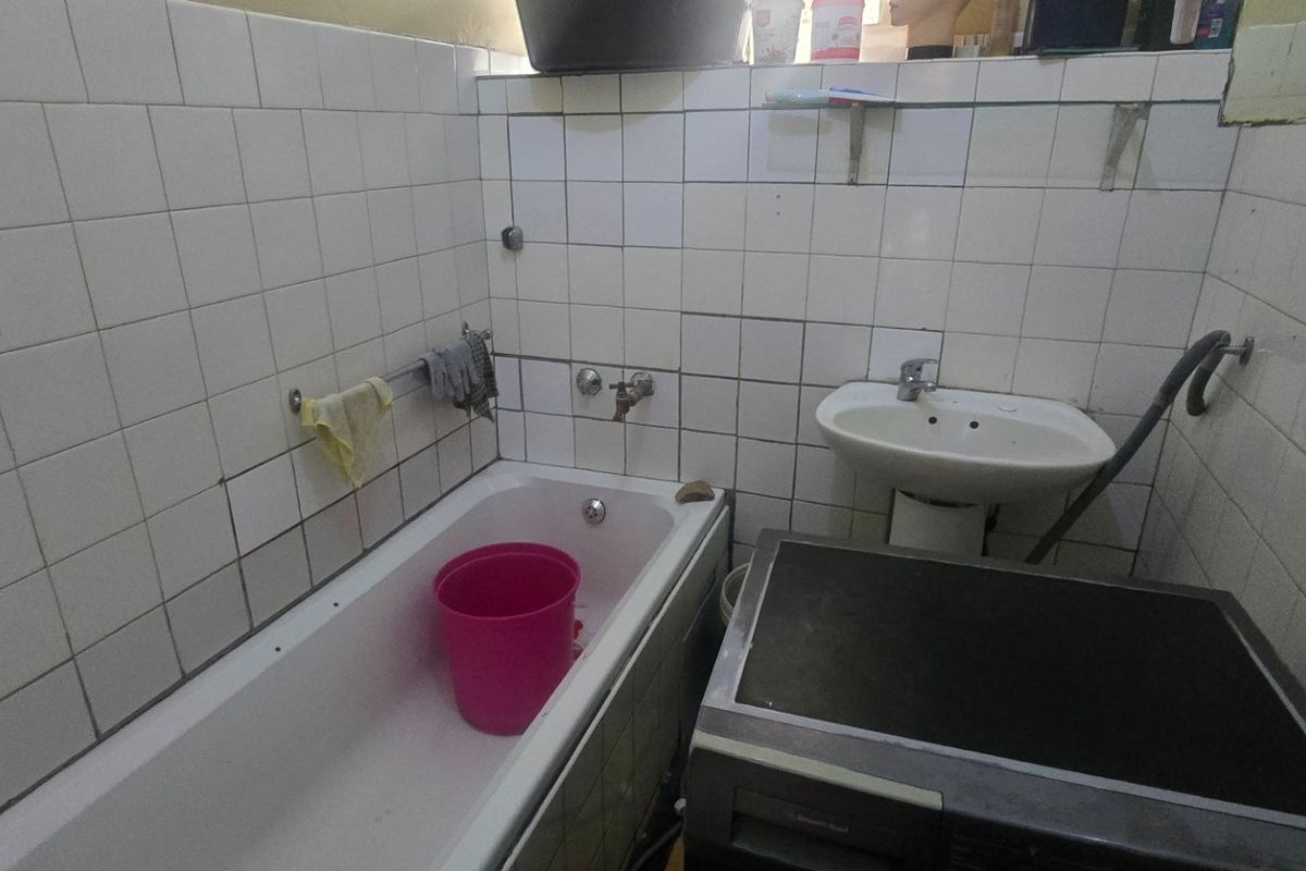 A compact bathroom featuring a bathtub and pedestal basin with wall tiling that requires maintenance and repair.