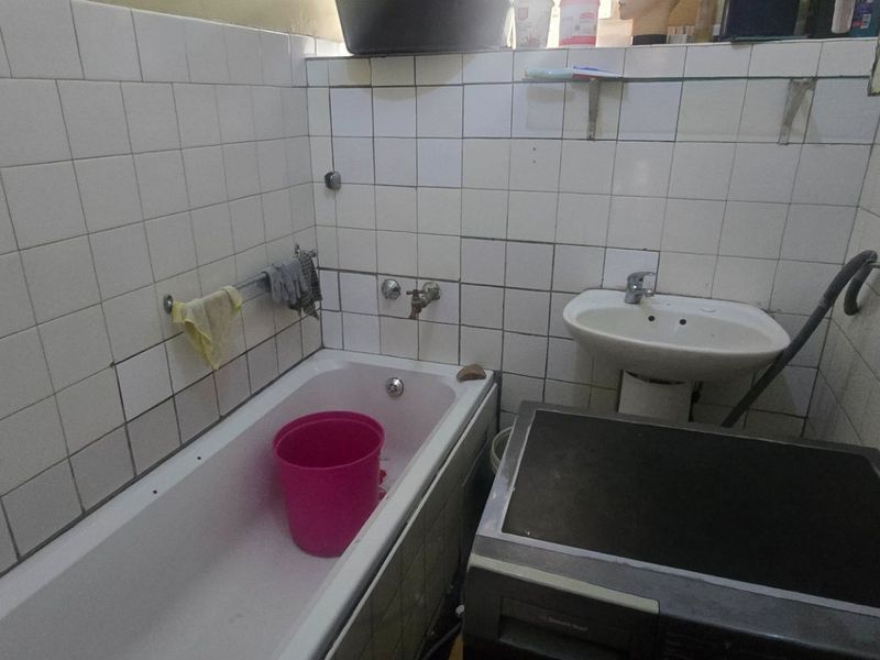 A compact bathroom featuring a bathtub and pedestal basin with wall tiling that requires maintenance and repair.