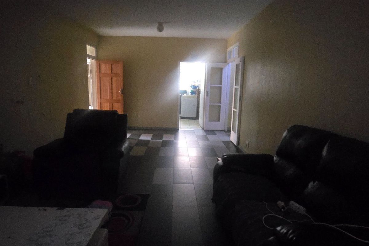 A dimly lit living room area featuring tiled flooring and access to adjacent rooms, requiring improved lighting and cosmetic updates.