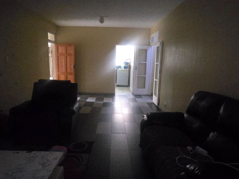 A dimly lit living room area featuring tiled flooring and access to adjacent rooms, requiring improved lighting and cosmetic updates.