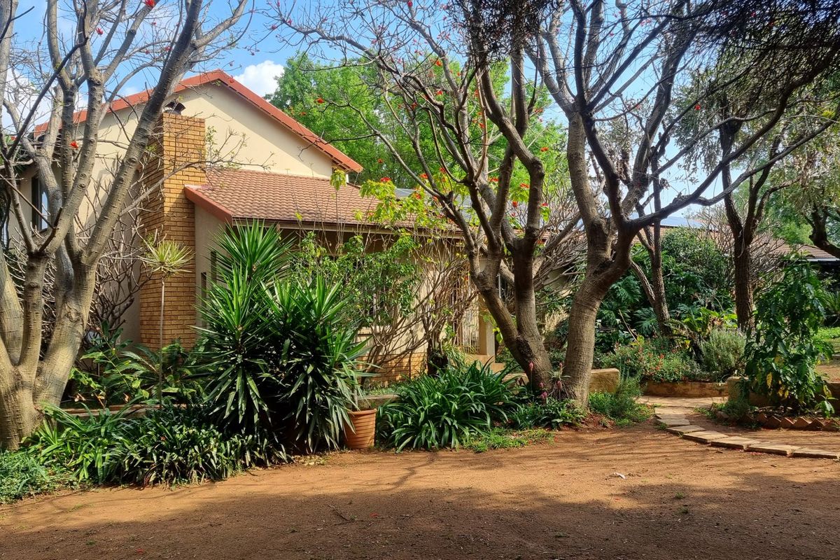 A view of the rear exterior of the house featuring a brick chimney, tiled roof, and a mature landscaped garden with a stone pathway.
