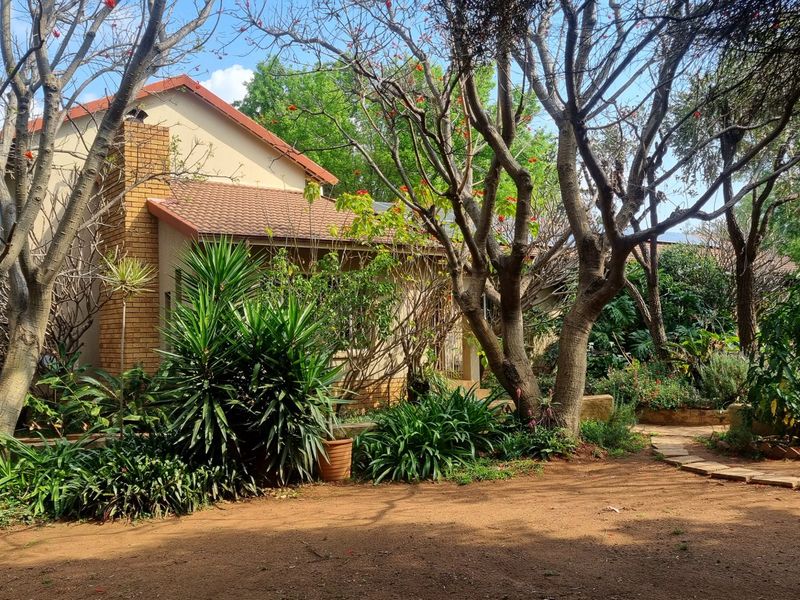 A view of the rear exterior of the house featuring a brick chimney, tiled roof, and a mature landscaped garden with a stone pathway.