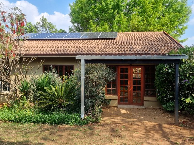 Rear view of the house featuring a paved patio, timber-framed glass doors, and roof-mounted solar panels set within a landscaped garden.