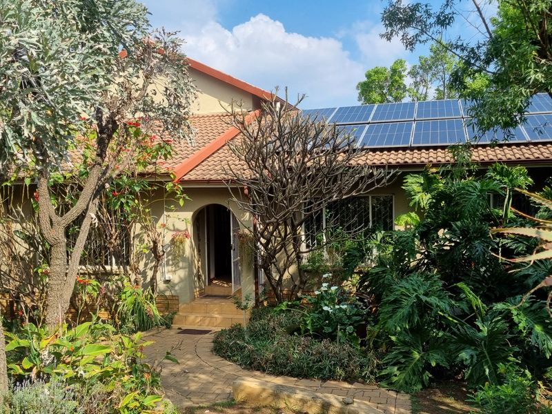 Front elevation of a house featuring a tiled roof with installed solar panels, surrounded by established garden landscaping and a paved entrance path.