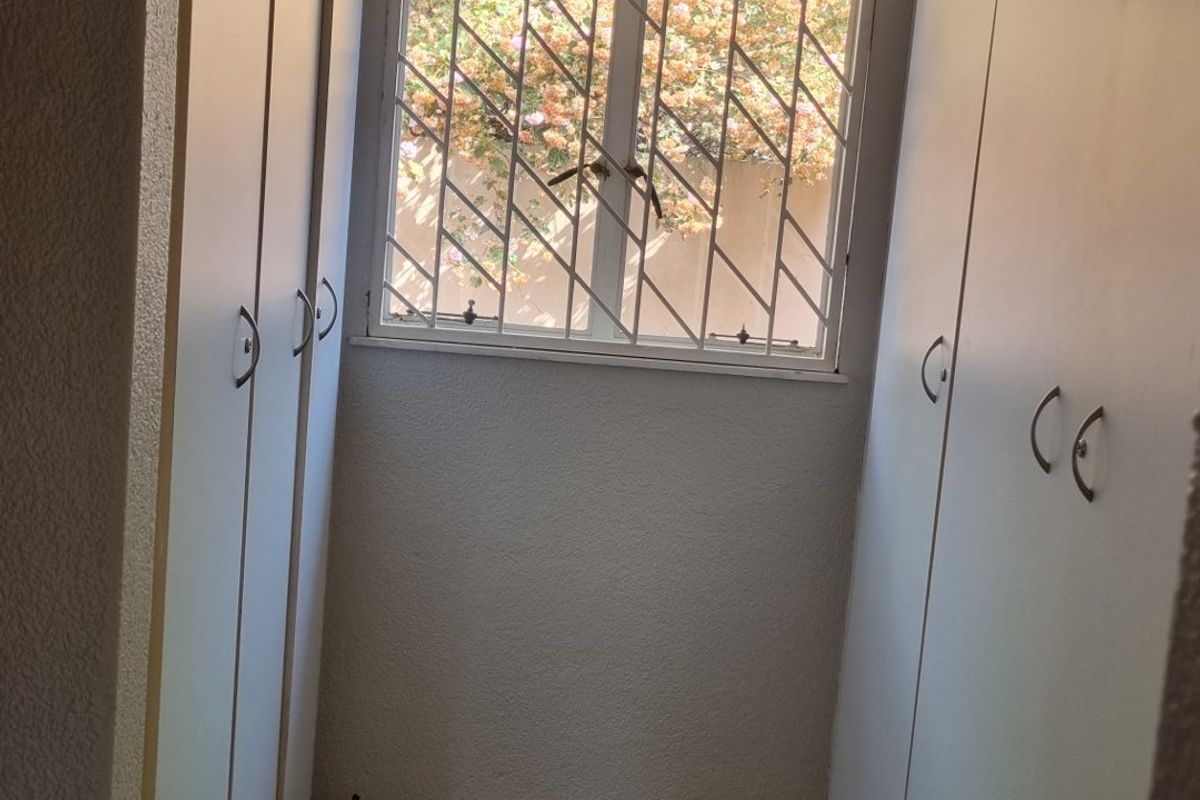 A clean, empty bedroom walk-in closet area featuring ample built-in cupboard storage, tiled flooring, and a window with security bars.