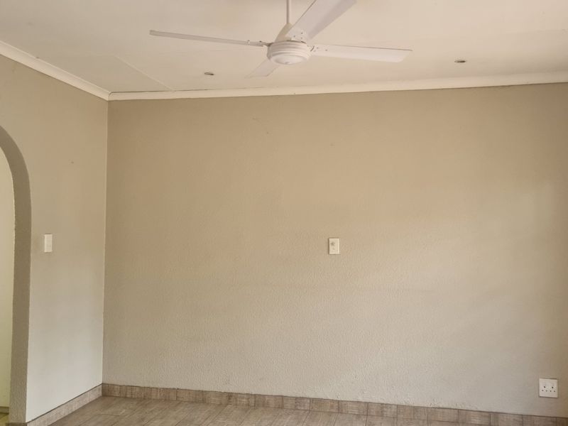 An empty living room featuring tiled floors, a ceiling fan, and a distinctive arched doorway, providing a neutral canvas for interior design.