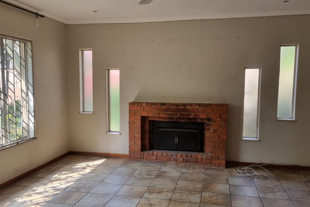 Spacious living room featuring a classic brick fireplace, tiled flooring, and large windows with security bars, offering a blank canvas for interior design.