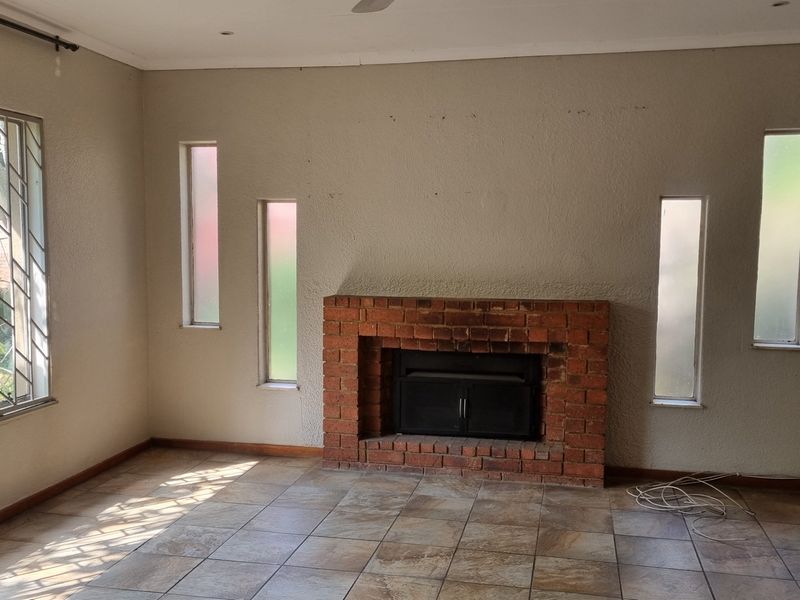 Spacious living room featuring a classic brick fireplace, tiled flooring, and large windows with security bars, offering a blank canvas for interior design.