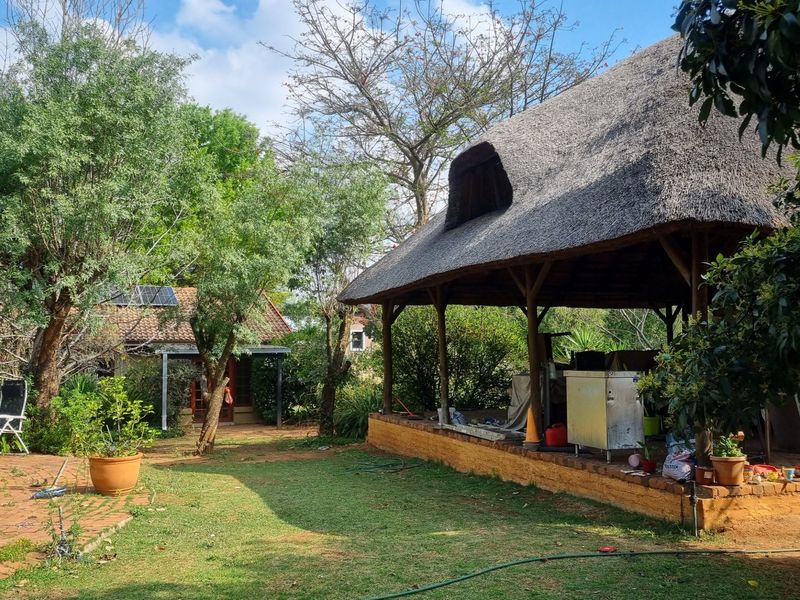 Outdoor thatched lapa area featuring a brick base and timber support posts, set within a garden environment with brick paving.