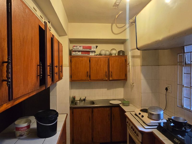 A compact kitchen featuring dated wooden cabinetry, a stainless steel sink, tiled backsplash, and built-in cooking appliances with security bars on the window.