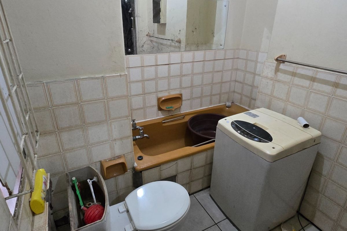 A dated bathroom featuring a bathtub, toilet, and tiled wall finishes. The space requires renovation to update the fixtures and address wall surface wear.