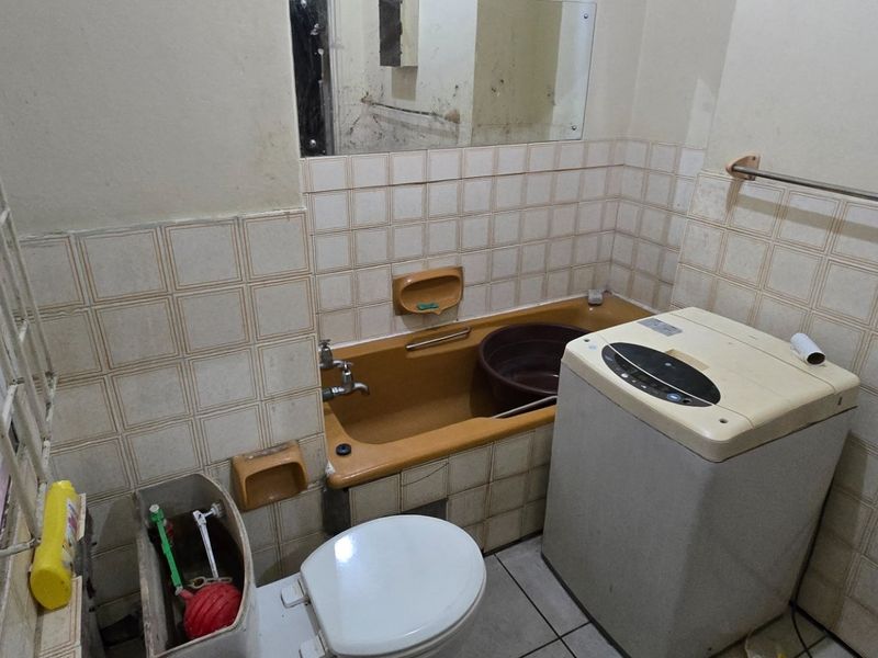 A dated bathroom featuring a bathtub, toilet, and tiled wall finishes. The space requires renovation to update the fixtures and address wall surface wear.