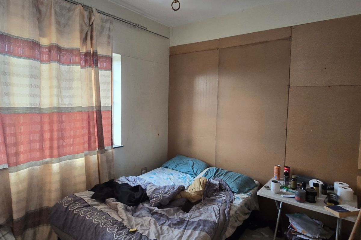 A bedroom featuring unfinished wall paneling and a window with curtain rails, requiring cosmetic updates to improve the overall finish and appeal.