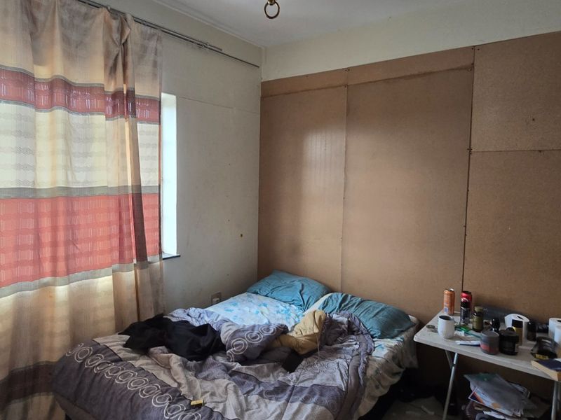 A bedroom featuring unfinished wall paneling and a window with curtain rails, requiring cosmetic updates to improve the overall finish and appeal.