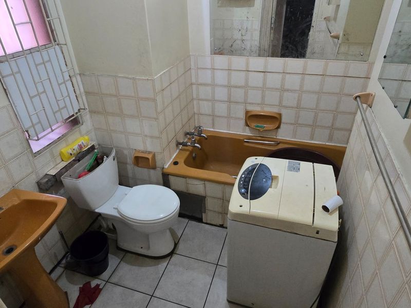 A dated bathroom featuring a pedestal basin, bathtub, and toilet with original wall tiling and security bars on the window.