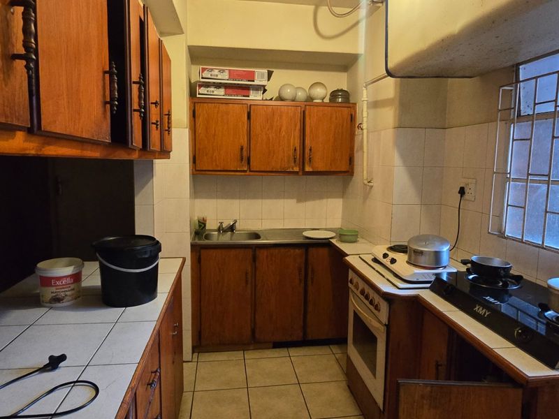A functional kitchen featuring wooden cabinetry, tiled countertops, and a built-in oven with gas hob, offering potential for modern renovation.