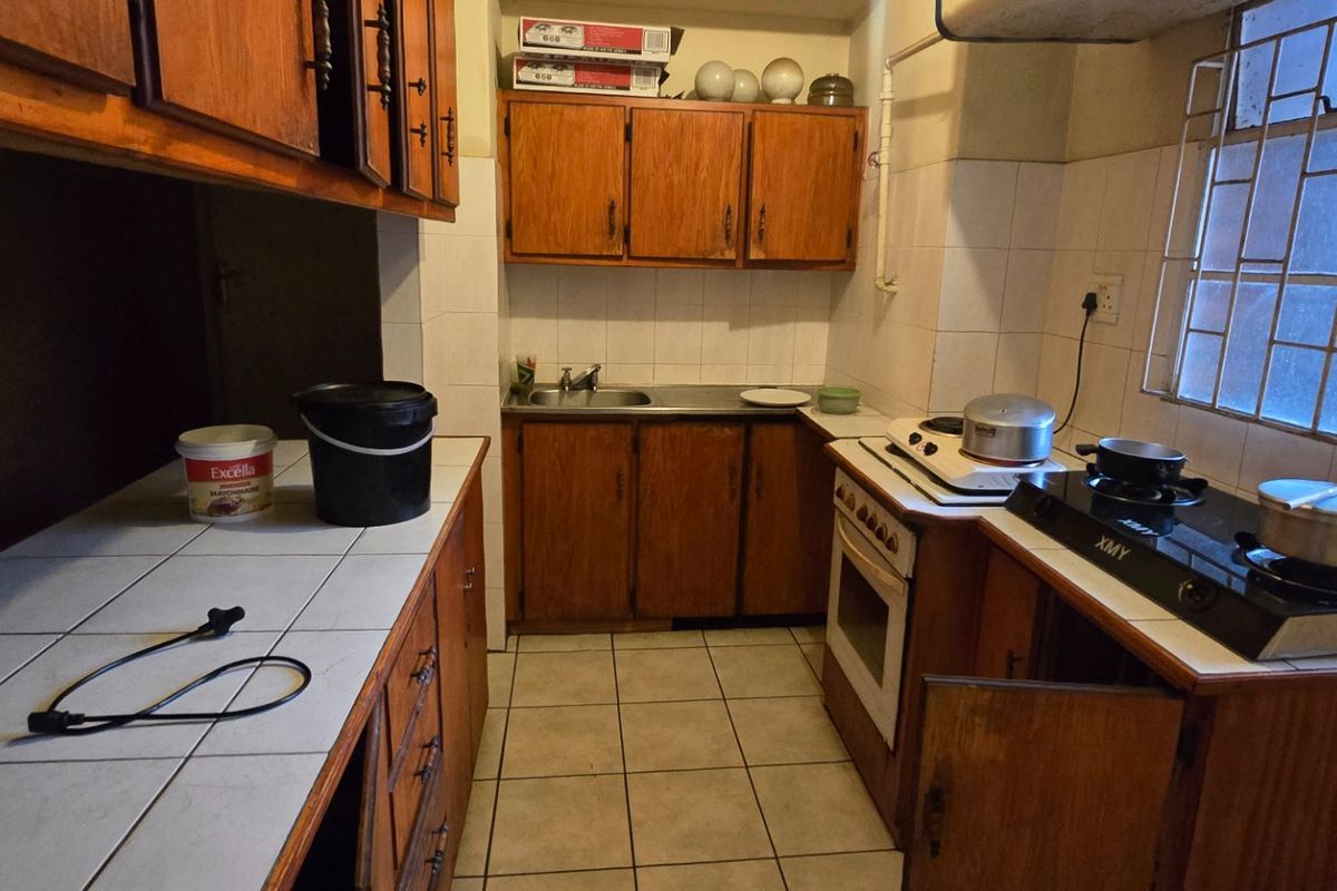 A functional kitchen featuring wooden cabinetry, tiled countertops, a built-in oven, and a gas hob, with security bars on the window.