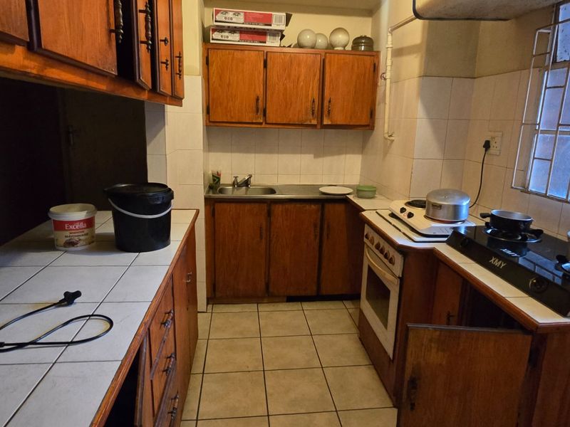 A functional kitchen featuring wooden cabinetry, tiled countertops, a built-in oven, and a gas hob, with security bars on the window.