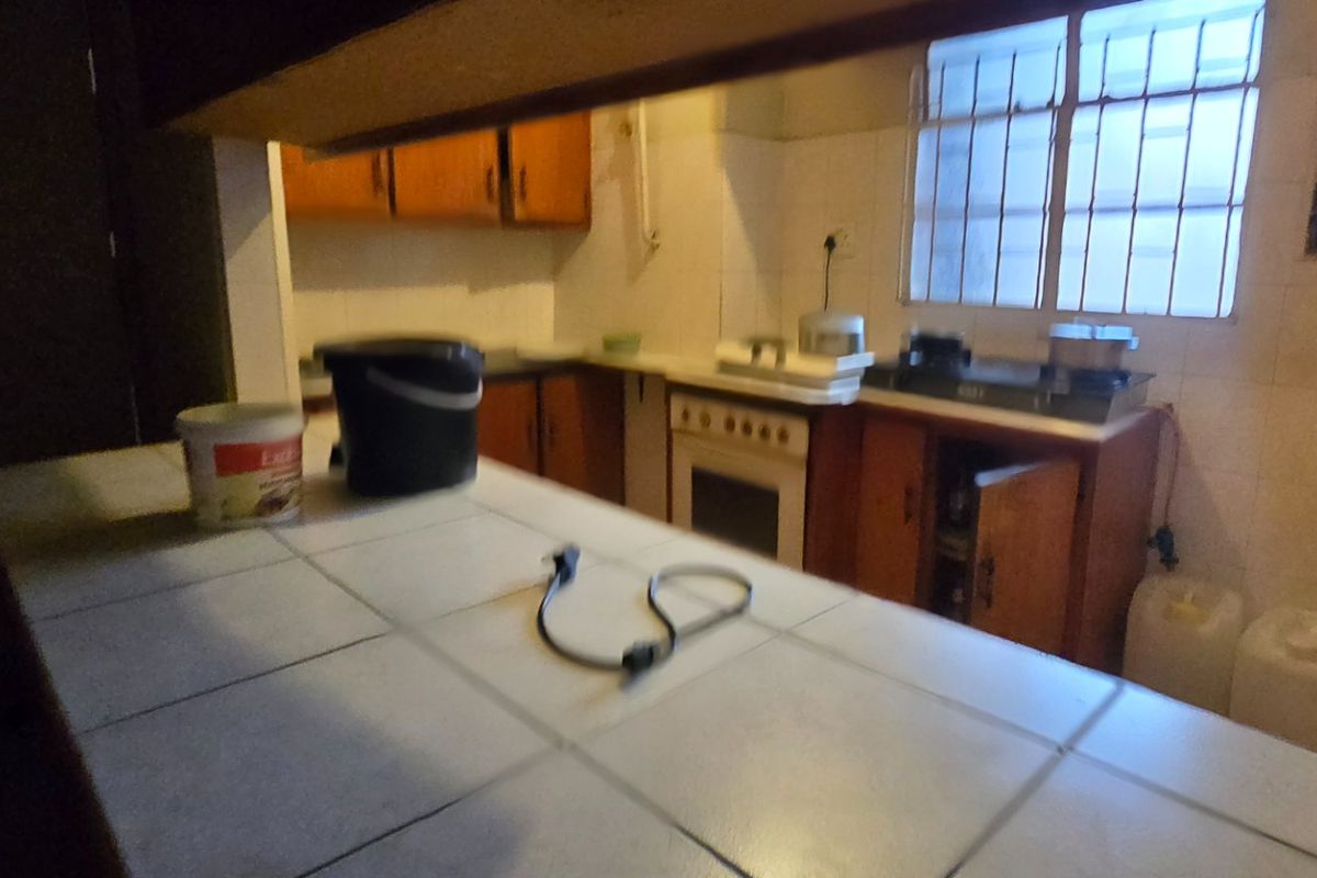 A dated kitchen featuring tiled countertops, built-in wooden cabinetry, and a freestanding stove, requiring modernization to improve functionality and aesthetic appeal.