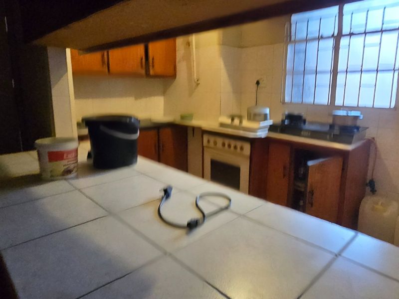 A dated kitchen featuring tiled countertops, built-in wooden cabinetry, and a freestanding stove, requiring modernization to improve functionality and aesthetic appeal.