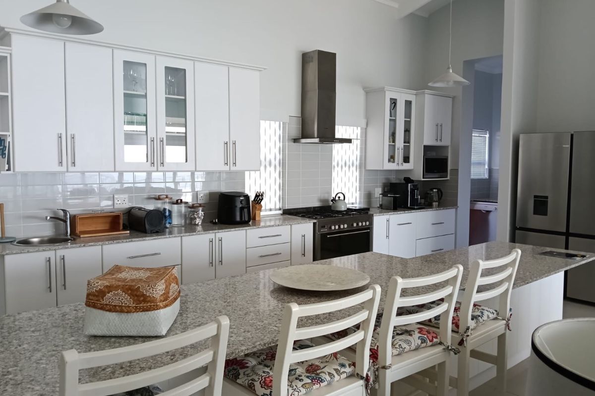 Modern kitchen featuring white cabinetry, granite countertops, a gas hob with stainless steel extractor, and a spacious breakfast island.