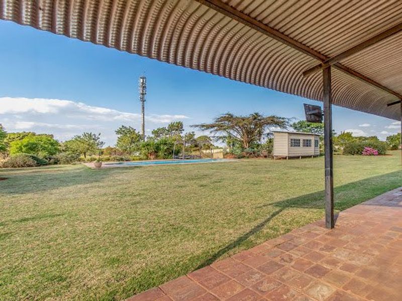 A covered patio area overlooking a spacious garden with a swimming pool and a small outbuilding.