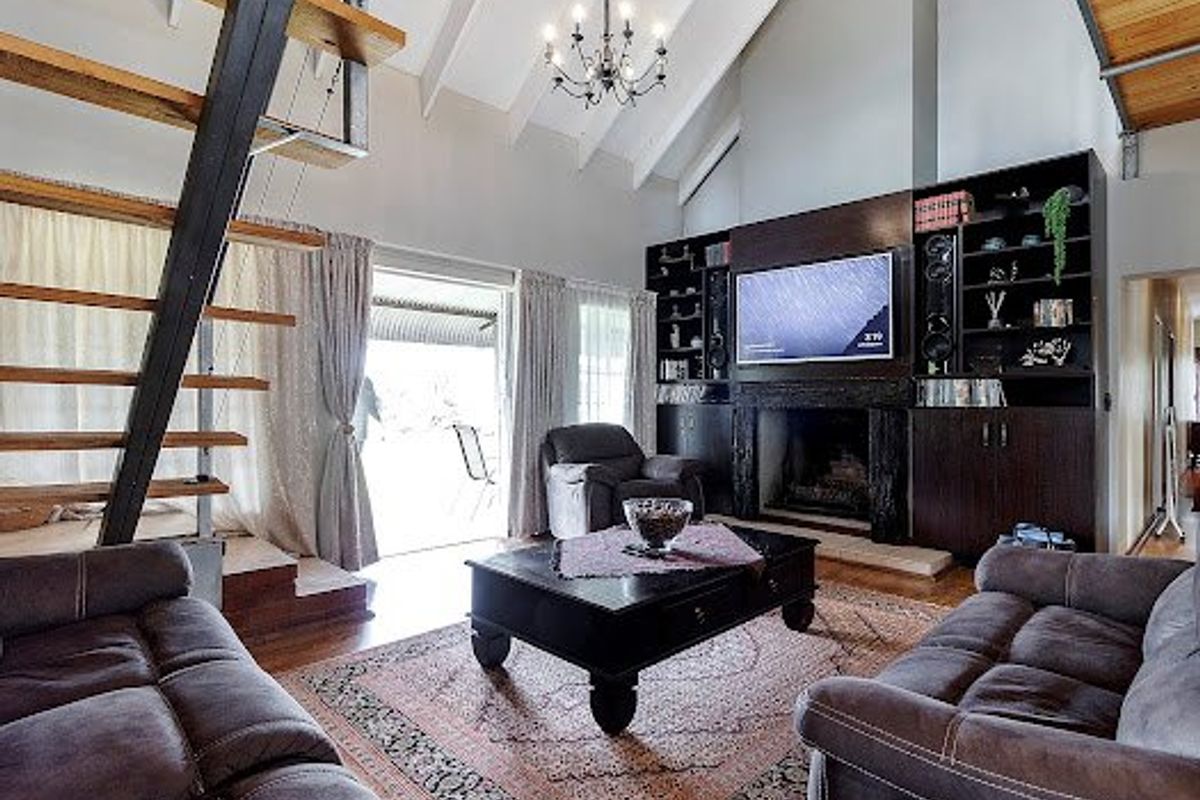 Spacious living room featuring a vaulted ceiling with exposed beams, a built-in fireplace with integrated cabinetry, and a striking timber staircase.