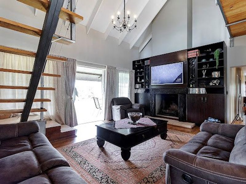 Spacious living room featuring a vaulted ceiling with exposed beams, a built-in fireplace with integrated cabinetry, and a striking timber staircase.