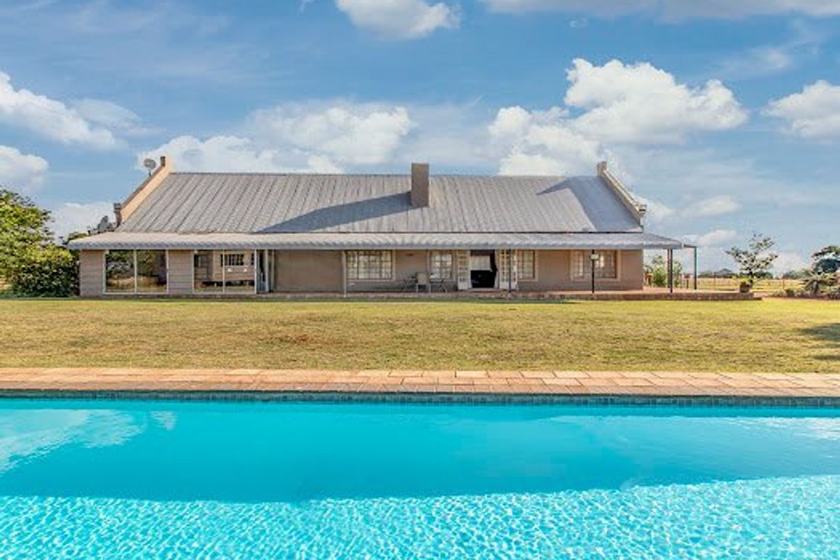 Rear view of the house featuring a large swimming pool, expansive lawn, and a covered patio area with sliding glass doors.