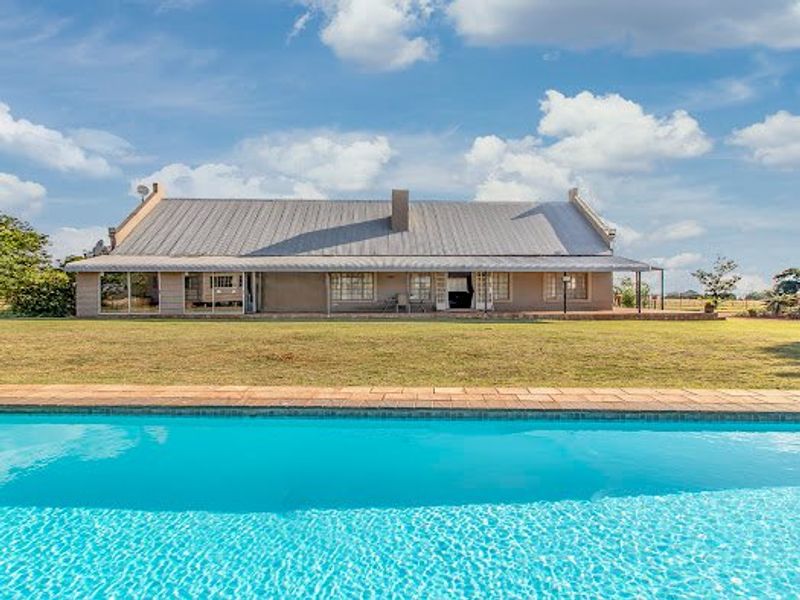 Rear view of the house featuring a large swimming pool, expansive lawn, and a covered patio area with sliding glass doors.