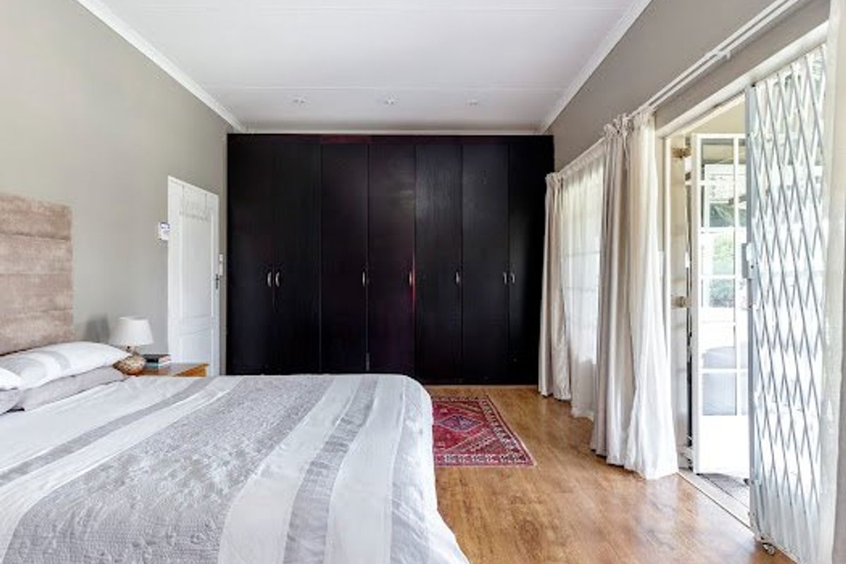 Spacious bedroom featuring dark built-in cupboards, laminate flooring, and direct access to the outdoors through a sliding door with a security gate.