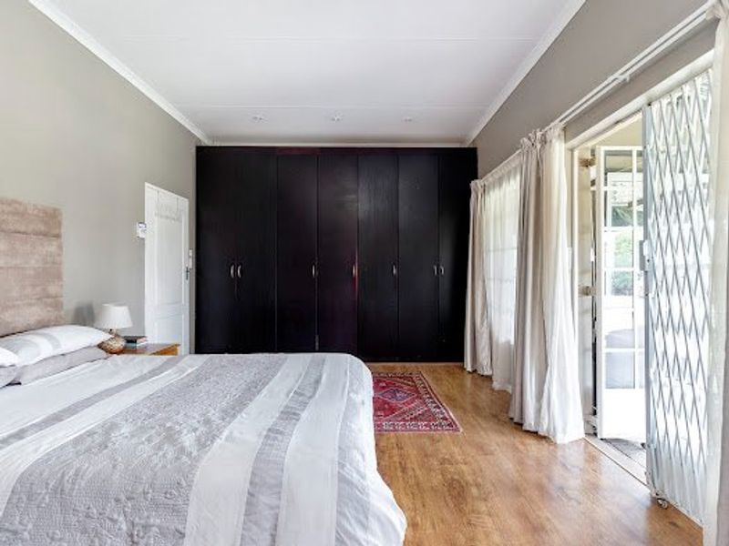 Spacious bedroom featuring dark built-in cupboards, laminate flooring, and direct access to the outdoors through a sliding door with a security gate.
