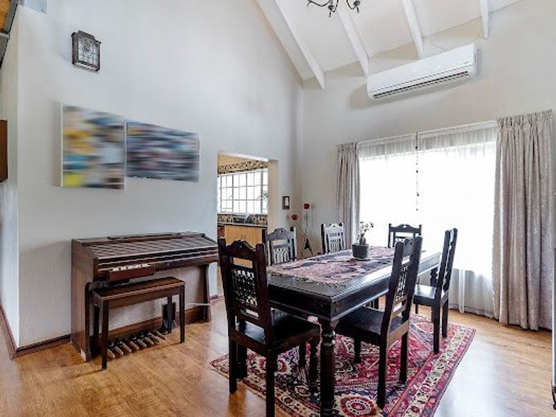 A bright dining room featuring vaulted ceilings with exposed beams, laminate flooring, and a wall-mounted air conditioning unit.