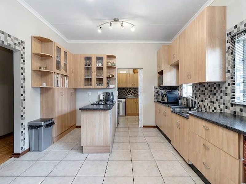 A functional kitchen featuring light wood-finish cabinetry, granite countertops, and a mosaic tile backsplash, with an adjoining scullery area visible through the doorway.