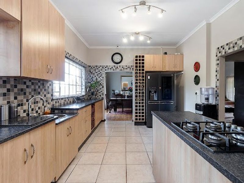 Spacious kitchen featuring light wood cabinetry, dark laminate countertops, mosaic tile backsplash, and a central island with a built-in gas cooktop.