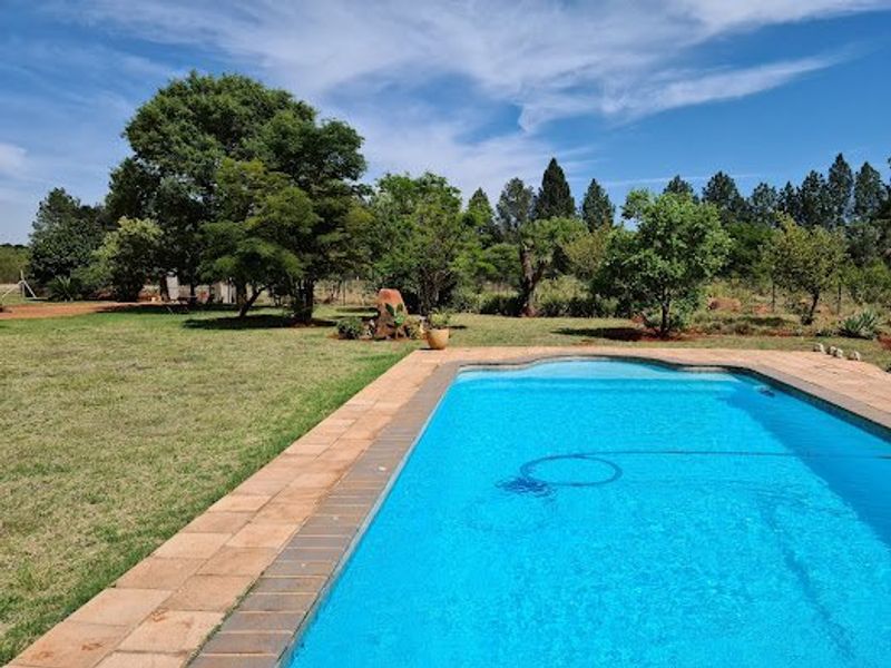 A well-maintained swimming pool with a paved surround, set within a spacious, landscaped garden area.