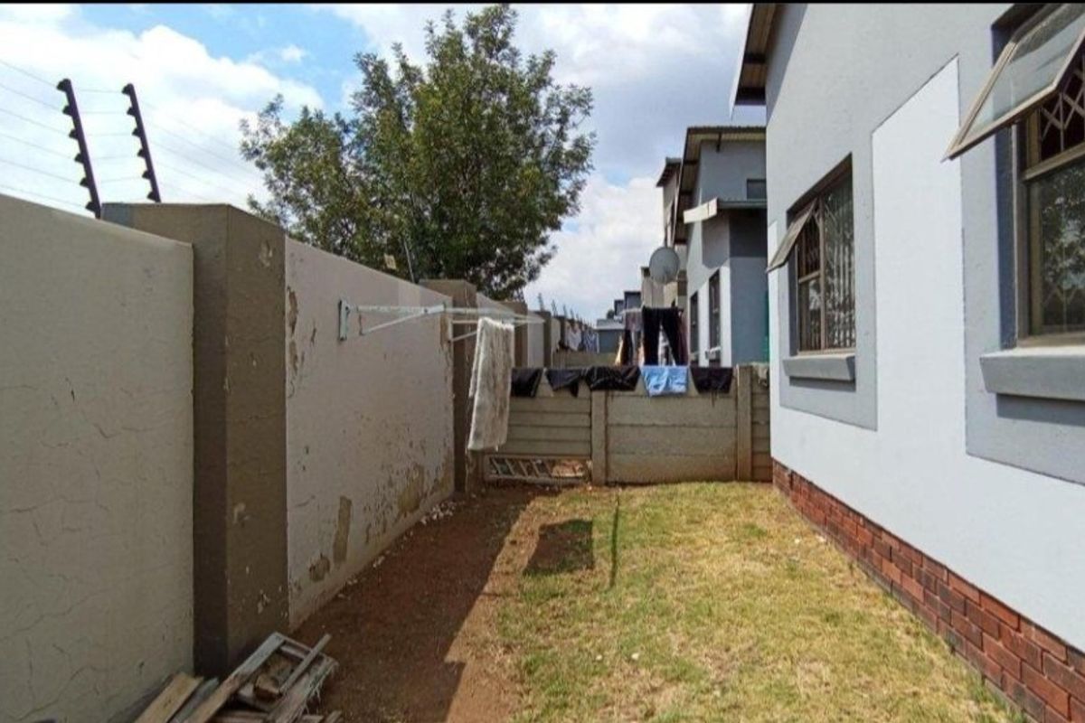 Rear exterior view of the property featuring a lawn, boundary wall with electric fencing, and brick-based exterior wall finish.