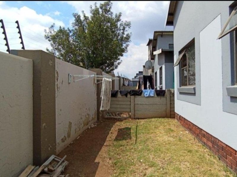 Rear exterior view of the property featuring a lawn, boundary wall with electric fencing, and brick-based exterior wall finish.