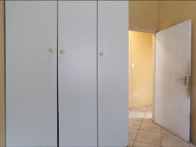 A bedroom interior featuring a built-in wardrobe and tiled flooring, showing signs of wear on the door and walls.