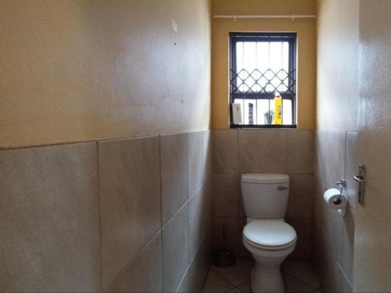 A compact, functional bathroom featuring tiled walls, tiled flooring, and a standard toilet with a window protected by security bars.