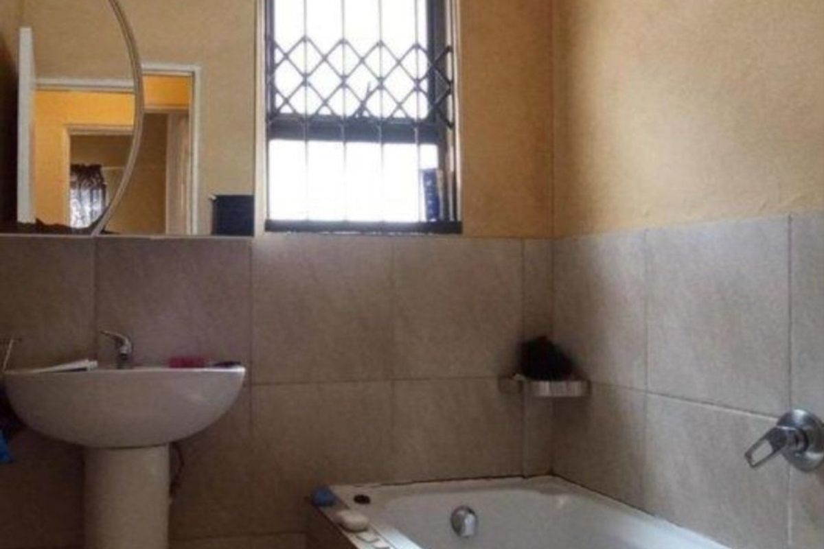A functional bathroom featuring a pedestal basin, bathtub with wall-mounted mixer, and tiled wall finishes with a security-gated window.