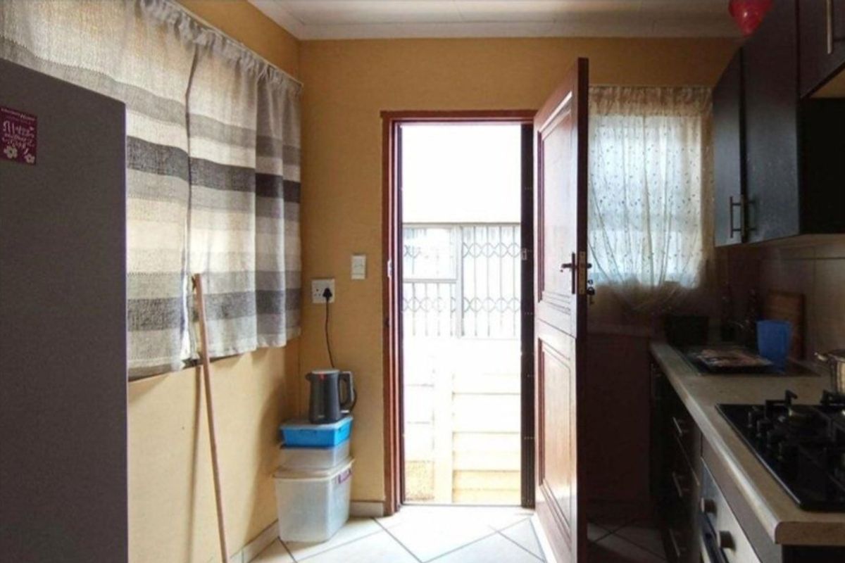 A functional kitchen featuring built-in cabinetry, a gas hob, and an oven, with direct access to an exterior area through a security gate.