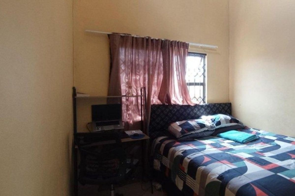 A compact bedroom featuring a window with security bars and a curtain rod, providing basic accommodation space.