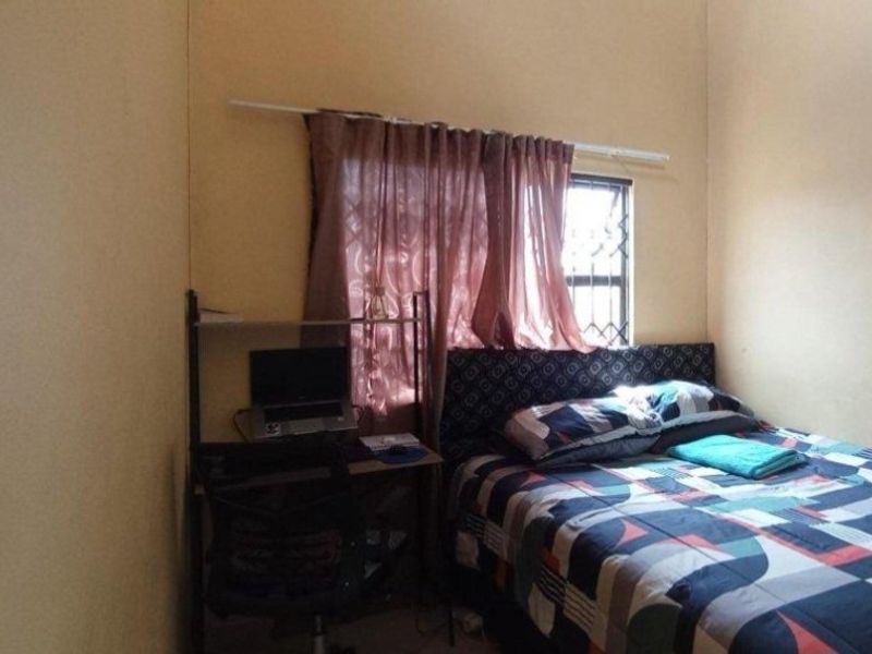 A compact bedroom featuring a window with security bars and a curtain rod, providing basic accommodation space.